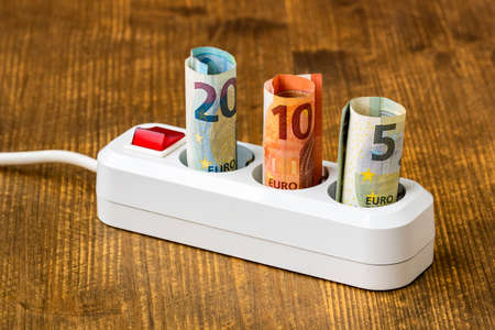 Rising energy costs concept. Euro money banknotes plugged into a white power strip. High energy...