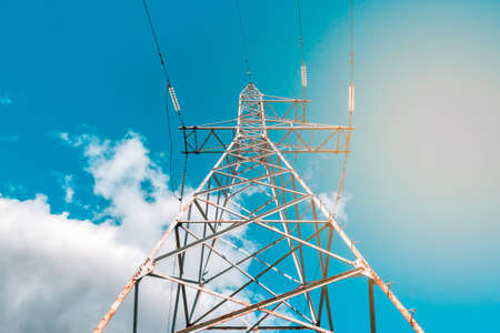 High voltage tower with electricity transmission power lines against blue sky, low angle viewの写真素材