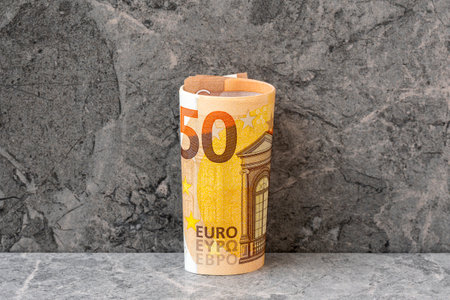 Roll of fifty euro banknotes on the grey stone backgroundの写真素材