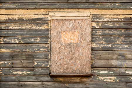 An old wooden window boarded up with plywood on a wooden wall. Easy way to repair windows of a poor...
