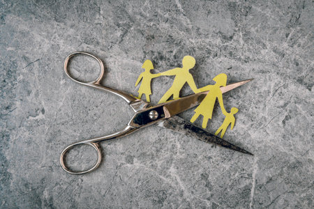 Divorce concept. A family made of paper with a figurine cutting off with scissors.