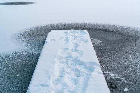 Pier and a freshly frozen lake. Fresh snow and thin ice.