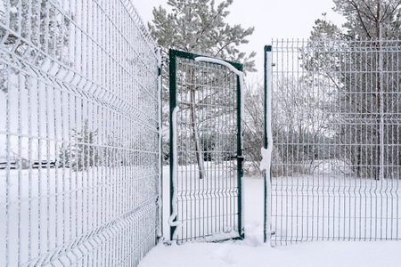 Hoarfrost covered metal fence with open door. Cold winter season.