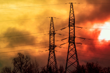 Electric power transmission lines in a dark smoke and fire light. High voltage post. Industrial...
