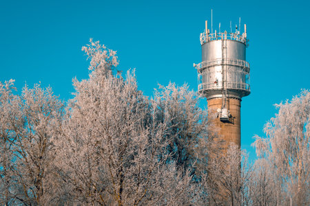 Water tower with communication antennas over a winter tree tops. Hoarfrost on the branches of trees.の写真素材
