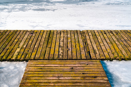 Old wooden pier on the side of a frozen lake on a warm day with snow meltingの写真素材