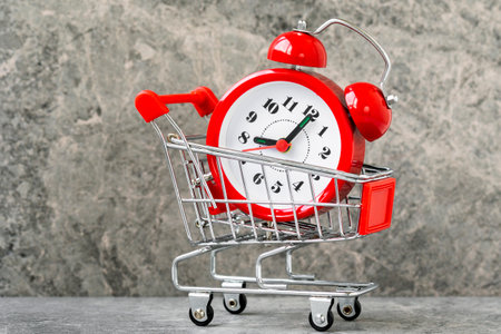 A metal supermarket trolley with alarm clock inside. Grocery supermarket, food and eats online buying and delivery concept. Start of discounts or sale.の写真素材