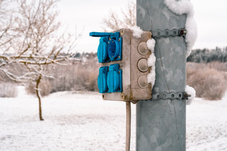 Outdoor power plug socket box with cover on the steel pole. Winter season.