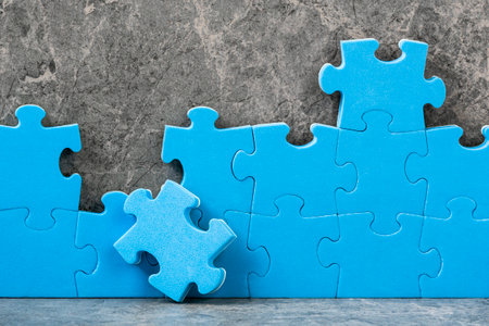 Unfinished blue jigsaw puzzle pieces on grey cement background. Team business concept.の写真素材