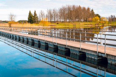 Long wooden pontoon bridge going to small island of lake. Pedestrian bridge on the lake.の写真素材