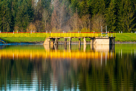 Landscape with a yellow metallic bridge construction and concrete spillway. Sunny spring day.の写真素材