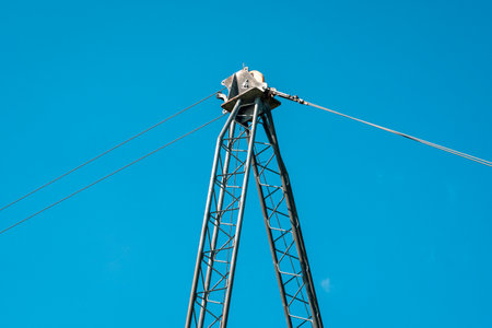 Device of a cableway. Metal support with roller mechanism and steel ropes with blue sky background.