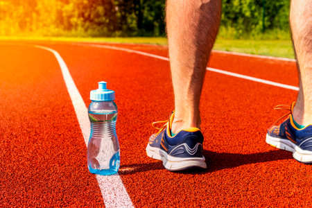 Runner in sneakers standing near water bottle on a running track. Sport activity on warm sunny day.の写真素材