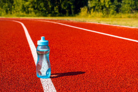 A sport water bottle on a running track outside.The Importance of Water While Exercising. Drink more water.の写真素材