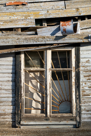 Old broken window with metal grid. Wall of abandoned wooden house.の写真素材