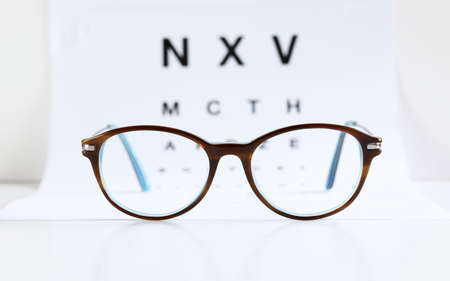 Closeup of eyeglasses and eye chart on white background