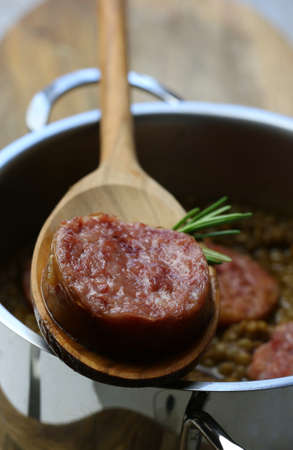 New Year's Eve Meal Italian Style. Top view of a slice of sausage (pork sausage) and rosemary on spoon. Background with pot with lentils.の写真素材