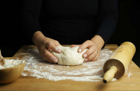 Preparing traditional homemade dough. Close up view of woman hands making fresh bread for pizza on a floured tableの写真素材