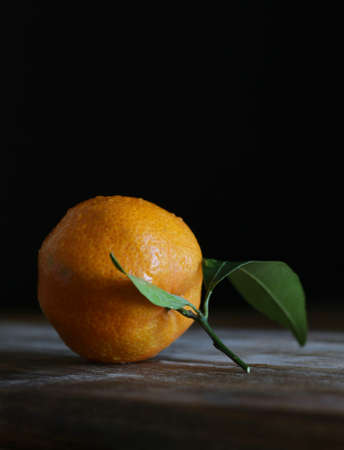 Close up of single fresh mandarin with leaf on wooden tableの写真素材