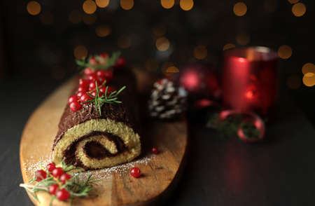 Chocolate Christmas Yule Log, Buche de Noel on wooden cutting board. Christmas decoration on dark...
