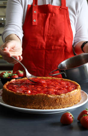 Homemade dessert concept. Woman hand decorating with strawberry sauce a strawberry cheesecake. Closeup.の写真素材