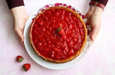 Homemade sweets concept. Woman hands holds a plate with strawberry cheesecake. Top view.