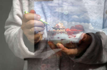 Breakfast during Covid 19. Woman take breakfast holding a bowl with yogurt, cereals and berries in...