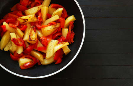 Homemade food concept. Potatoes and peppers side dish in a pan. Dark wooden background.Top view.