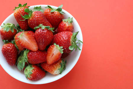 Concept of healthy fruits. Fresh strawberries in a white bowl isolated on red background. Top view.の写真素材