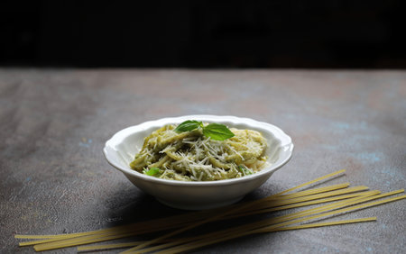Pasta spaghetti with pesto sauce and fresh basil leaves. Dark background. Selective focus