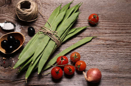 Piattoni green beans, tomatoes, onion and black olives isolated on wooden background. Jackdaws. Top...