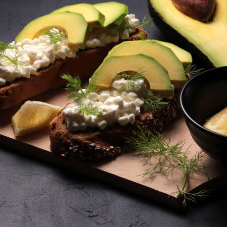 Healthy appetizer with cereal bread, avocado and cottage cheese on dark background. Top view. Copy space.の写真素材