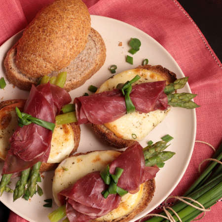 Bresaola and asparagus rolls with cheese and toasted bread on dark background. Healthy food. View...