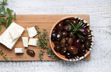 Black olives, feta cheese and aromatic herbs on wooden cutting board. Directly above.の写真素材