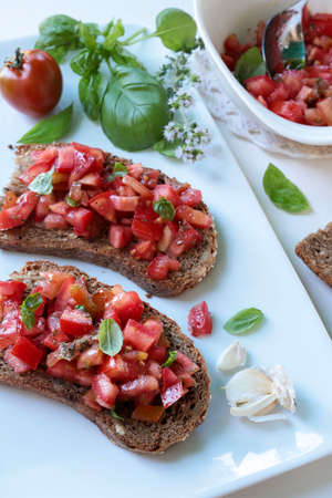 Italian appetizer or starter. Bruschetta with tomato, fresh basil, garlic, oregano and olive oil on white plate. Directly above.の写真素材