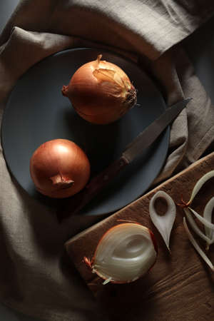 Onions on wooden chopping board on dark background. Directly above.の写真素材