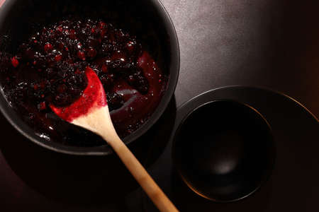 Raspberry and blueberry jam in a pot on dark background. Making jam at home. Homemade preserve.