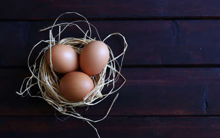 Many chicken eggs on dark light. Wooden background, directly above.