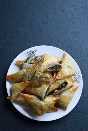 Traditional Greek cuisine. Spanakopita, crispy phyllo pastry triangles with spinach and feta on gray...