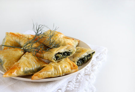 Traditional Greek cuisine. Spanakopita, crispy phyllo pastry triangles with spinach, feta, dill and Tzatziki sauce on white background Directly above.の写真素材