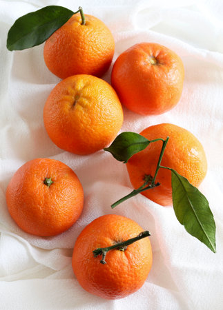 Ripe tangerines with leaves on white cloth, closeupの写真素材