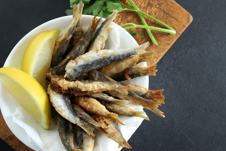 Fried fish with lemon and parsley on a black background.
