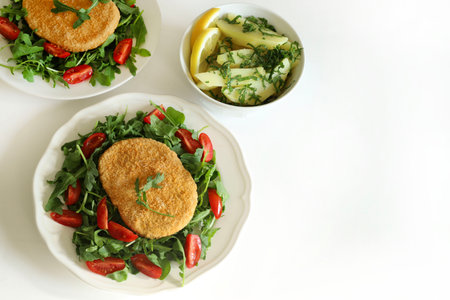 Soy meat cutlet with fresh rocket, slice tomatoes in a white plate and potatoes with parsley, white background. Healthy, vegan and vegetarian food.の写真素材