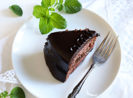 Sachertorte (chocolate sacher cake) - slice on a white plate, mint leaves decoration, white background. Traditional Austrian dessert. Copy space.の写真素材