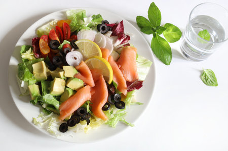 Salad with smoked salmon, avocado, olives, lemon, lettuce and fresh vegetables on a white plate. Healthy food. Directly above.の写真素材