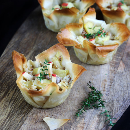 Phyllo pastry baskets filled with gorgonzola, apples, and walnuts on a wooden background. Overhead...