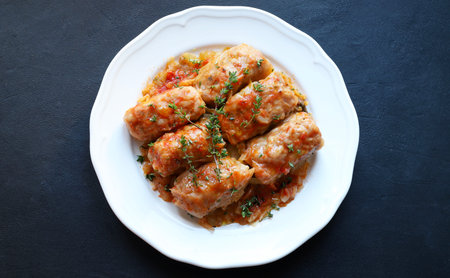 A white plate of cabbage rolls with a meat and rice filling, topped with thyme leaves, on a dark...