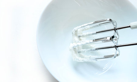 Two metal whisks immersed in a creamy, white mixture inside a white bowl. Concept of creation....
