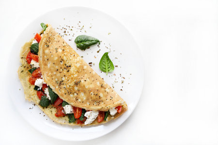 Savory omelet stuffed with fresh spinach, cherry tomatoes, and cheese on a white plate, white background. French dish. Copy space.の写真素材