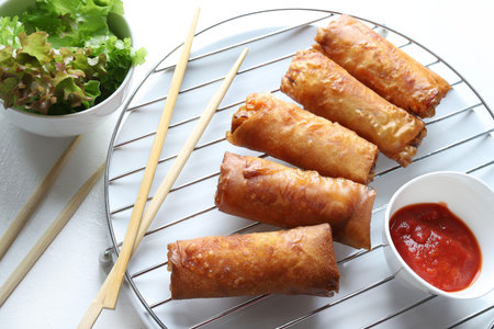 Fried spring rolls with sauce and chopsticks on a white background